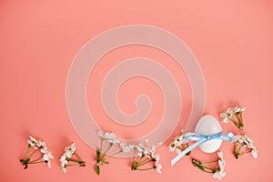 White flowers and an egg with a blue ribbon on a pink background. Easter background, a place to copy. Flat lay.