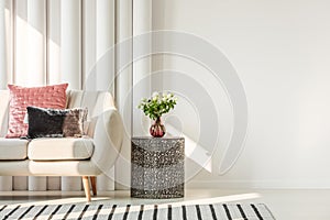 Flowers on glass vase on stylish table next to white sofa with pastel pink and black velvet pillows, real photo with copy