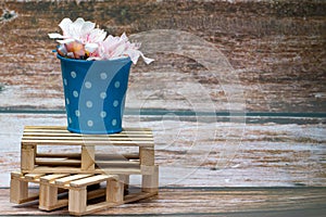 White flowers inside a blue metal bucket with white polka dots on a wooden pallet. Wild flowers.
