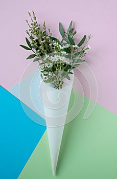 White flowers in paus tracing paper cone on colored paper background photo