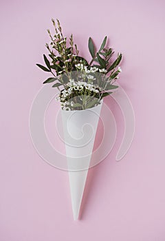 White flowers in paus tracing paper cone on pink background photo