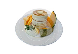 White fluffy pancake and butter topping on white ceramic plate decorated with yellow and green melon and smooth wipping cream