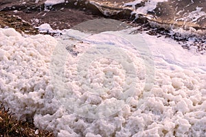 White foam accumulations on the shore near the water surface texture background, foam aggregates, scum, river froth, cumulus foam