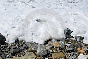 White foam from the big storm waves on the sea pebble coast.