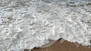 white foam in waves covers sandy beach