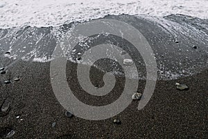 White foam waves wash over the dark lumpy beach