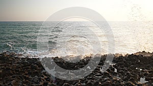 White foamy waves crashing on rocks outdoors at sunset. Wide shot landscape of stormy Mediterranean sea in sunshine