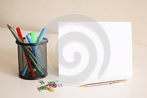 White folded sheet of paper on the table. Nearby are pens and pencils.