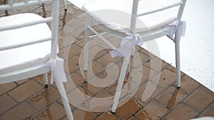 White folding chairs at the wedding ceremony with drops from the rain. Wet seat in the open air