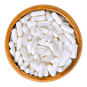 White food supplement capsules in wooden bowl over white photo