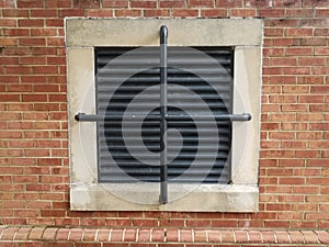 White frame with black bars on red brick wall and ventilation vent