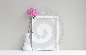 White frame, empty mock-up, beside vase with pink aster