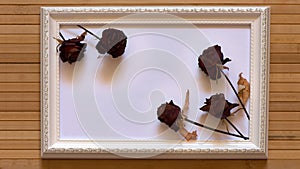 White frame with five dried red roses and empty white canvas on natural bamboo wall.