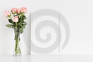 White frame mockup with a bouquet of pink roses in a glass vase on a white table. Portrait orientation