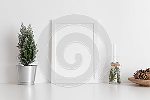 White frame mockup with a cypress tree, candles and pine cones on a white table. Christmas decoration