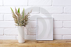 White frame mockup with grass and green leaves in cylinder vase