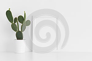 White frame mockup with a opuntia cactus in a pot on a white table. Portrait orientation