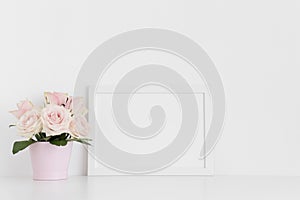 White frame mockup with pink roses in a pot on a white table.Landscape orientation