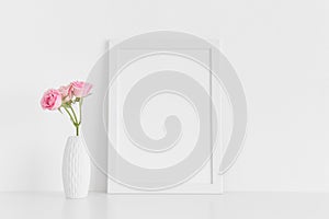 White frame mockup with pink roses in a vase on a white table.Portrait orientation