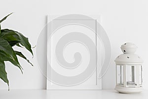 White frame mockup with a spathiphyllum and candle holder on a white table. Portrait orientation
