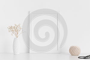 White frame mockup with workspace accessories  and gypshophila in a vase on a white table.Portrait orientation