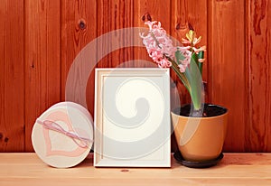 White frame, pink hyacinth flower in brown pot and gift box on wooden background.