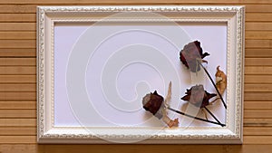 White frame with three dried red roses and empty white canvas on natural bamboo wall.