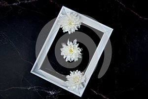 A white frame with three white flowers on a dark marble background inside