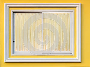 White frame window in yellow wall with curtain.