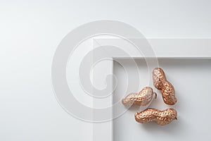 White framed minimalist composition of gold peanuts on white background with copy space for text.