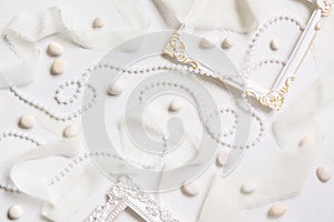 White frames, pearls, pebbles and silk ribbons top view on a white table