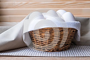 White fresh raw eggs lie on a white napkin in a small rough rustic basket