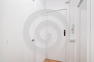White front door to apartment with intercom on wall. There is peephole in door for observing what is happening outside
