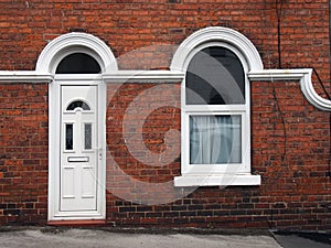 White front door and window of a typical old brick british terraced house with white decorative paintwork