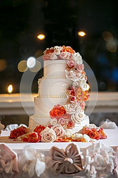 White frosting wedding cake with orange and white roses on a ceremonial table