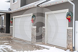 White garage doors of home with festive wreaths mounted on the gray wall