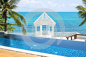 White gazebo on the blue sea with a swimming pool in the foreground. Rest and relaxation on the sea coast