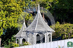 White gazebos two in park or outdoor schoolyard with pointy spires with white fence and background green trees