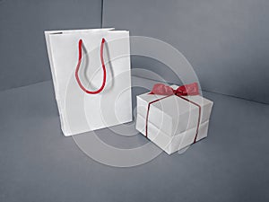 White gift bag with red handles and a white square box with red bow. Mockup box and paper package for overlaying a pattern,