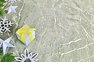 White gift box with arborvitae branches and snow flake origami on grey marble background.