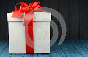White gift box with a big red bow on a blue wooden background