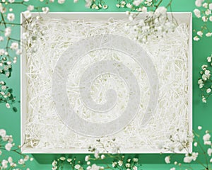 White gift box with decorative straws fillers on green background with flowers