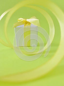 White gift box at the end of the spiral yellow ribbon, green background, vertical.