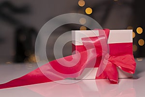 White gift box with pink ribbon bow on gold bokeh background