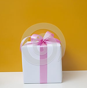 White gift box with pink ribbon isolated on orange background.