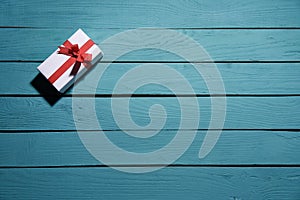 White gift box with red bow on blue wooden planks