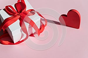 white Gift box with red bow ribbon and red heart on pink background for Valentines day.Happy birthday, wedding, greeting