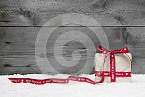 White gift box with red long ribbon and bow on grey wooden background