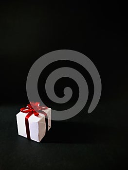 A white gift box with red ribbon on black background. Vertical..