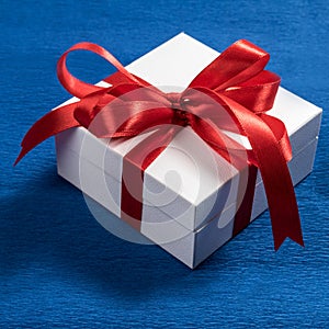 White gift box with red ribbon on blue background